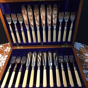 May include: A wooden box with a blue velvet lining containing a set of silver knives and forks with ivory handles. The box has a brass latch and the inscription "Elkington & Co. Ltd. Birmingham" on the bottom.