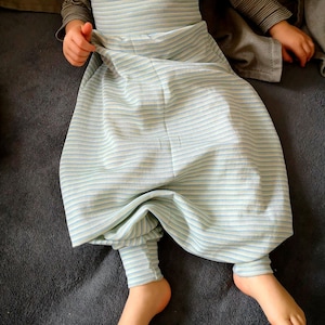 Könnte beinhalten: Ein Kind trägt einen gestreiften Schlafsack mit einem hellblauen und weißen Muster. Der Schlafsack ist aus weichem, bequemem Stoff und hat eine lockere Passform.