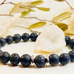 May include: Black lava rock beaded bracelet with silver spacer beads. The bracelet is on a white surface with white crystal clusters.