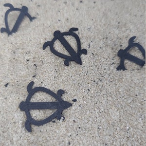 May include: Four black turtle-shaped charms on a white sandy surface.