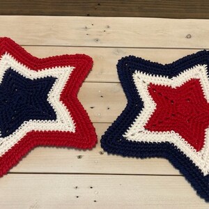 May include: Two crocheted stars in red, white, and blue. The stars are layered with a white star in the center, a red star around the white star, and a blue star around the red star.