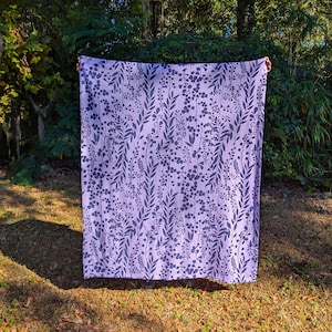 May include: A purple throw blanket with a dark blue floral pattern. The blanket is made of a soft, comfortable fabric and is perfect for adding a touch of elegance to any room.