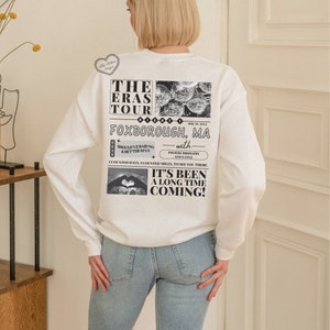 May include: White sweatshirt with a black and white graphic print of a concert poster for "The Eras Tour" with the text "Foxborough, MA" and "It's Been A Long Time Coming!"