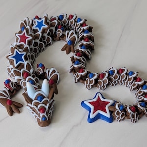 May include: A brown articulated dragon figurine featuring a repeating scale pattern with white outlines. The dragon is decorated with red and blue star-shaped accents and small red and blue conical spikes along its body, head, and tail.