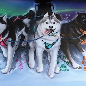 May include: A colorful painting of four huskies pulling a sled. The dogs are running on a snowy surface with a green, blue, and purple aurora borealis in the background. The dogs are named Kira, Memphis, Eleanor, and the text "Stay Positive & Dream Big" is written on the image.