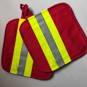 Könnte beinhalten: Zwei rote Topflappen mit gelben und silbernen reflektierenden Streifen. Jeder Topflappen hat unten rechts ein kleines Design mit einer Nähnadel und Faden.