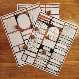 May include: Three character sheets for a role-playing game, featuring a portrait section, character details, and the word "ROGUE." The sheets have a red and black design with dice scattered across them. The sheets are on a wooden surface.