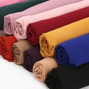 May include: A stack of 10 colourful scarves in various shades of pink, red, yellow, blue, brown, and green. The scarves are made of a soft, lightweight fabric and are rolled up neatly.