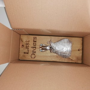 May include: A wooden sign with the text "Last Orders" is inside a cardboard box. A silver bell is attached to the sign and is wrapped in bubble wrap.