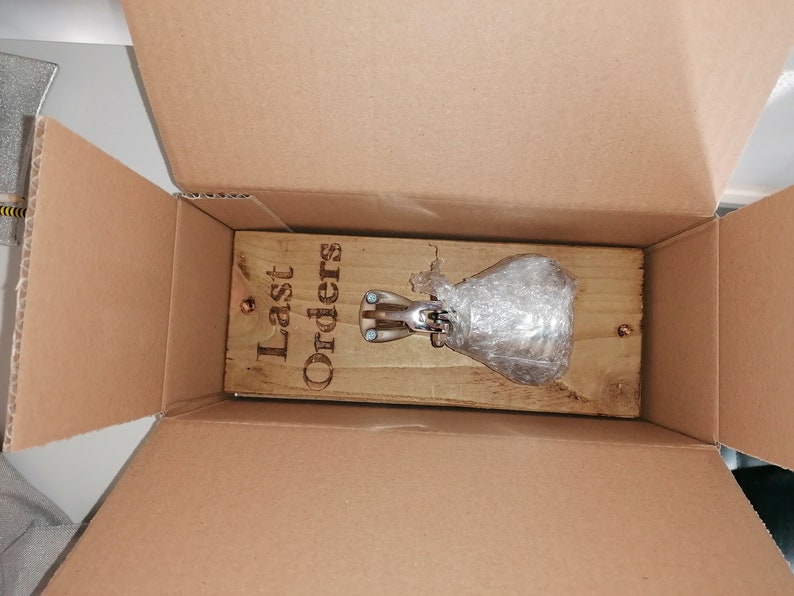 May include: A wooden sign with the text "Last Orders" is inside a cardboard box. A silver bell is attached to the sign and is wrapped in bubble wrap.