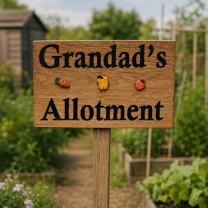 May include: A wooden sign with the words "Grandad's Allotment" in black. The sign features small, decorative vegetables and fruit. It is mounted on a wooden post in a garden, with a path and planting beds visible.