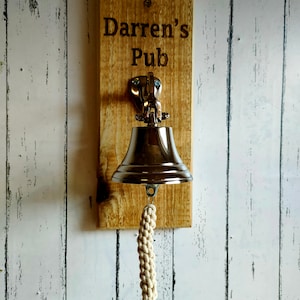 May include: A wooden sign with the text "Darren's Pub" engraved on it. A silver bell with a white rope hangs from the sign.