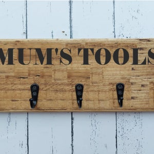 May include: A wooden wall-mounted key holder with five hooks and the text "MUM'S TOOLS" in black lettering.