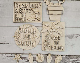 May include: A collection of unfinished wooden beach-themed Christmas ornaments. The ornaments include a sign that reads "Christmas is better at the beach", a bucket with a Christmas tree and shovel, a sign that reads "Sandy and Bright", and a sign that reads "Deck the Palms".