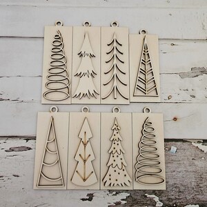 May include: Eight wooden Christmas tree ornaments with different designs. The ornaments are all unfinished and ready to be painted or decorated.