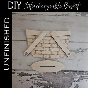 May include: An unfinished wooden DIY interchangeable basket cutout with a woven pattern design and two attached handles, accompanied by a separate oval wooden base piece with a centre slot for assembly. The text DIY Interchangeable Basket and UNFINISHED is visible.