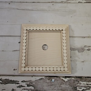 May include: A wooden frame with a beaded border and a circular cutout in the center. The frame is light brown and has a natural wood finish.