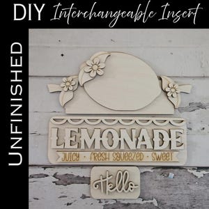 May include: Unfinished wooden DIY interchangeable insert set. Includes a lemon-shaped top piece with floral accents, a sign that reads "LEMONADE," and a small "Hello" sign. The sign also includes the words "Juicy, Fresh Squeezed, Sweet."