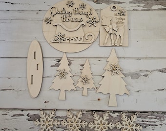 May include: Wooden Christmas craft kit with a sleigh, reindeer, trees, and snowflakes. The kit includes the text "Dashing through the snow" and "Where the treetops glisten".