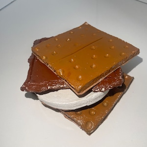 Op de afbeelding: Een stapel van drie grahamcracker-achtige vierkanten, een wit, een bruin en een beige, die lijken op een s'more.