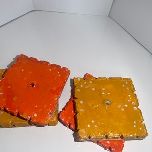 Op de afbeelding: Vier vierkante keramische onderzetters met een gespikkeld ontwerp. Twee onderzetters zijn oranje met witte stippen en twee zijn goud met witte stippen.