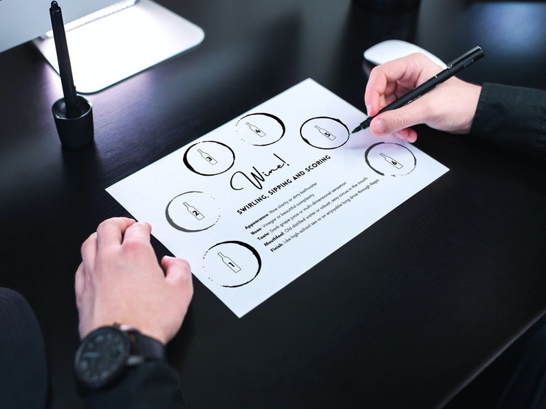 Op de afbeelding: Een wit vel papier met het woord "Wine!" en de tekst "Swirling, Sipping and Scoring" erop gedrukt. Er zijn zes cirkels met wijnflessen in elke cirkel. Een persoon gebruikt een zwarte pen om op het papier te markeren.