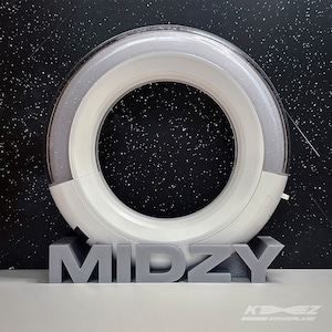 以下が含まれることがあります： 白いリングライトは、灰色のベースに「MIDZY」という文字が印刷されています。リングライトは、白い斑点のある黒い背景に設置されています。
