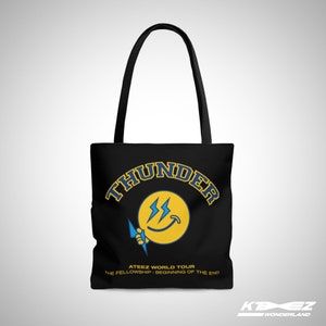 May include: Black tote bag featuring a yellow smiley face with lightning bolts and the text "THUNDER" in a blue and yellow arc above the smiley face. The text "ATEEZ WORLD TOUR THE FELLOWSHIP: BEGINNING OF THE END" is printed below the smiley face.