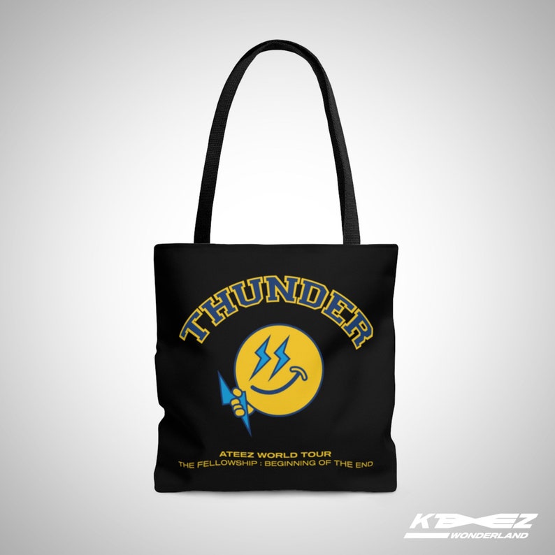 May include: Black tote bag featuring a yellow smiley face with lightning bolts and the text "THUNDER" in a blue and yellow arc above the smiley face. The text "ATEEZ WORLD TOUR THE FELLOWSHIP: BEGINNING OF THE END" is printed below the smiley face.