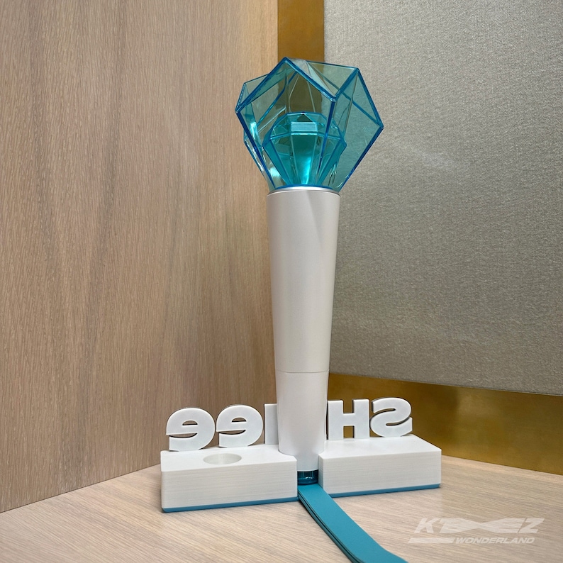 K&ouml;nnte beinhalten: Ein blauer und wei&szlig;er Lichtstick mit einer diamantf&ouml;rmigen Spitze. Der Lichtstick steht auf einem wei&szlig;en St&auml;nder mit dem Wort "SHINE" darauf.
