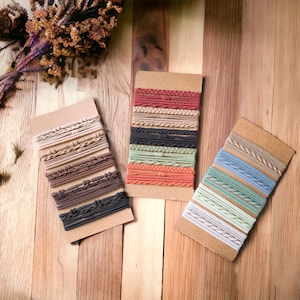 May include: Three sets of hair ties in various colours, including beige, brown, black, green, orange, blue, and white. Each set is arranged on a cardboard backing, showcasing different textures and styles of hair accessories.