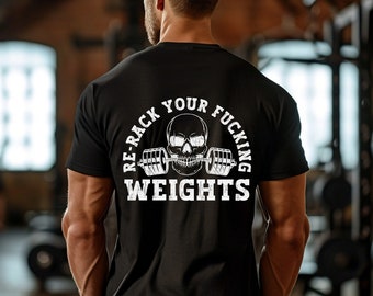 Puede incluir: Camiseta negra con un gráfico blanco de calavera y barra. El texto "Re-Rack Your Fucking Weights" está impreso en la parte posterior de la camiseta.