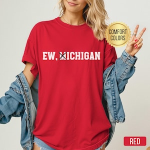 Peut inclure: T-shirt rouge avec l'inscription blanche "EW, XICHIGAN". Le t-shirt a des manches courtes et un col rond. Un autocollant doré avec les mots "COMFORT COLORS" est visible. Le mot "RED" est dans un rectangle rouge.