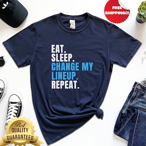 Op de afbeelding: Een marineblauw t-shirt met witte tekst die "EAT. SLEEP. CHANGE MY LINEUP. REPEAT." luidt.