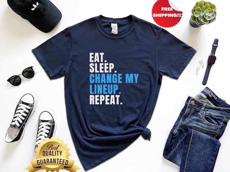Op de afbeelding: Een marineblauw t-shirt met witte tekst die "EAT. SLEEP. CHANGE MY LINEUP. REPEAT." luidt.