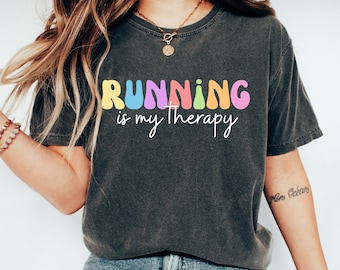 May include: A dark gray t-shirt with the text "RUNNING is my therapy" in colorful, rounded letters. The letters are outlined in black and have a rainbow color scheme.