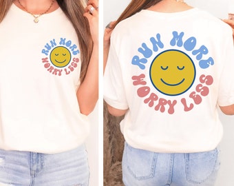 May include: White t-shirt with a blue and pink graphic that says "Run More Worry Less" with a yellow smiley face in the center.