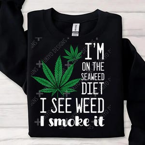 Könnte beinhalten: Schwarzes Sweatshirt mit einem großen grünen Cannabisblatt und dem weißen Text "I'M ON THE SEAWEED DIET I SEE WEED I smoke it". Marke Gildan.