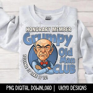 May include: A light gray sweatshirt with the words "HONORARY MEMBER Grumpy Old Man CLUB" in blue. The graphic features a grumpy-looking man with crossed arms and a red bow tie. The text "TELLING IT LIKE IT IS!" is also included.