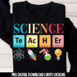 以下が含まれることがあります： カラフルな文字で「SCIENCE TEACHER」と書かれた黒いスウェットシャツ。デザインには、周期表の元素Te、Ac、H、Erと、ロケット、原子、フラスコ、電球などの科学をテーマにしたグラフィックが含まれています。