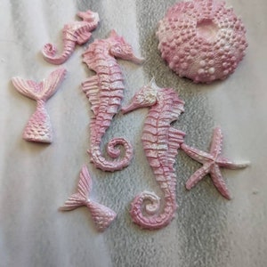May include: A set of pink seahorse cake decorations, including two large seahorses, a small seahorse, two mermaid tails, a starfish, and a pink sea urchin.