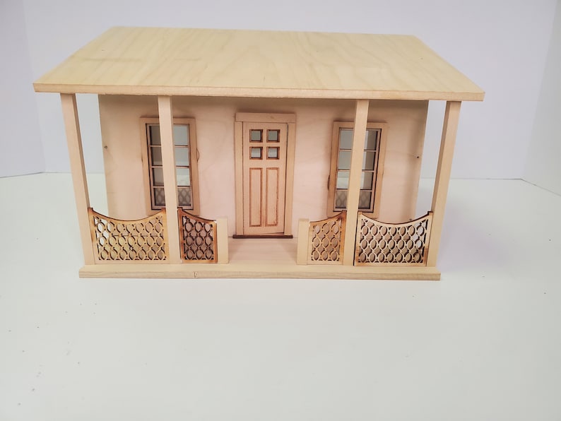 Peut inclure: Une maison de poup&eacute;e en bois avec un porche avant, deux fen&ecirc;tres et une porte. Le porche a une balustrade d&eacute;corative.