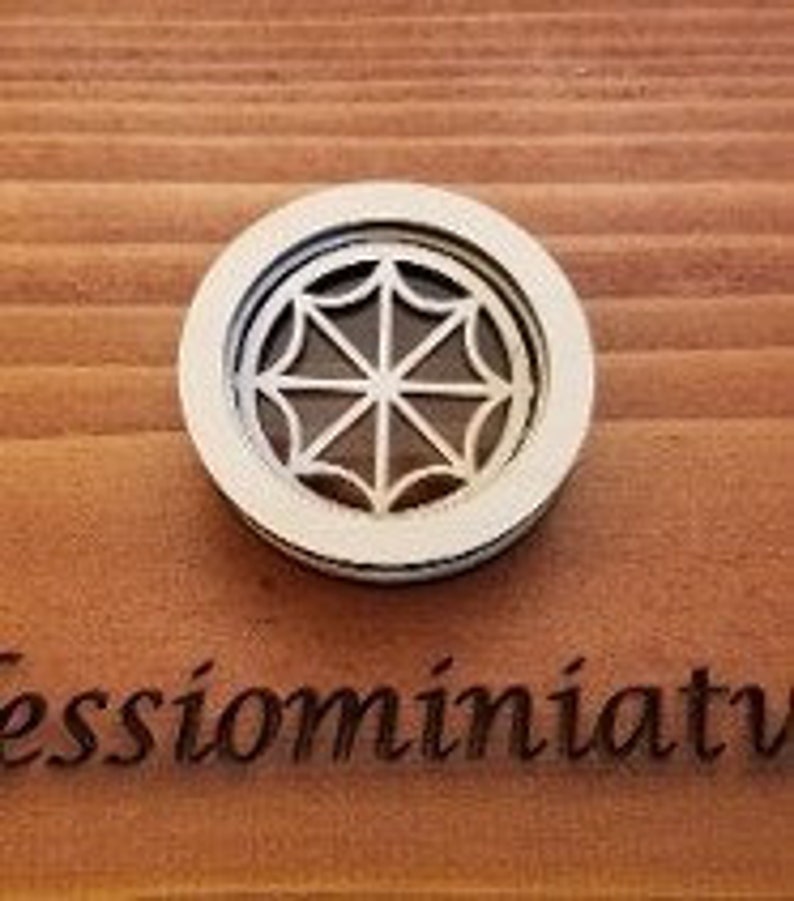 May include: A white wooden round window with a decorative design of eight spokes radiating from the center. The window is framed with a slightly wider white border.