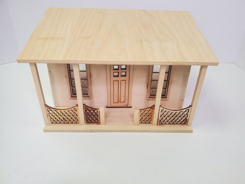 Peut inclure: Une maison de poup&eacute;e en bois avec un porche avant, deux fen&ecirc;tres et une porte. Le porche a une balustrade d&eacute;corative.