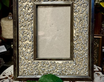 May include: A silver picture frame with a decorative floral design and rhinestones. The frame is made of wood and has a dark brown finish.