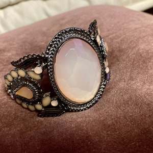 May include: A silver bracelet with a large, oval-shaped, white stone surrounded by smaller white stones and intricate silver detailing.