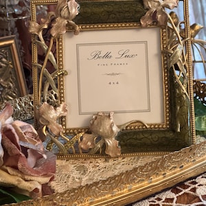 May include: A square Bella Lux fine frame with a dark green border featuring gold scrollwork and metallic floral accents. The frame includes a white insert with the text Bella Lux Fine Frames 4 x 4. The border is decorated with sculpted flower motifs.