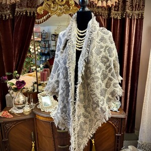 May include: A gray and white patterned scarf with a fringed edge, draped over a black mannequin. The scarf is displayed in a room with a vintage vanity and a mirror.