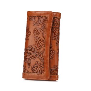 May include: A brown leather wallet with a floral embossed design. The wallet is folded and has a flap closure. The leather has a glossy finish and a warm, natural color.
