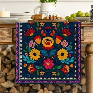May include: A rectangular table runner featuring a dark blue background with a vibrant, symmetrical floral pattern in shades of red, yellow, pink, and teal. The design includes a decorative border with geometric shapes in pink, white, and purple.